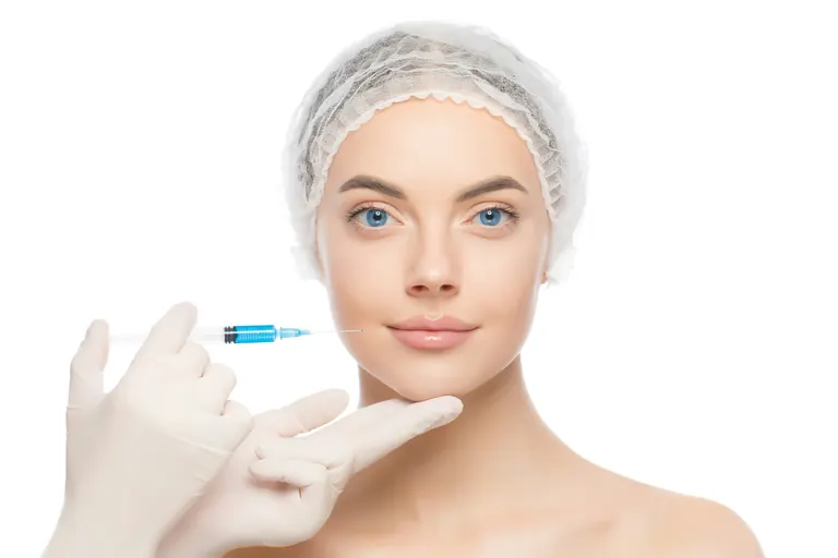 A gloved hand holding a fine syringe beside the cheek of a model against a white background