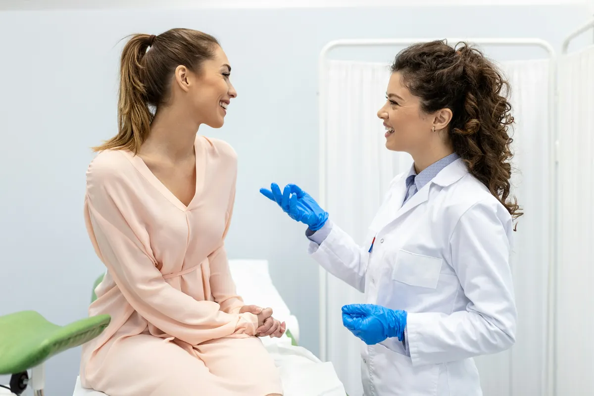 A patient holding a hand mirror while a gloved clinician steadies her jaw, reviewing the treated area