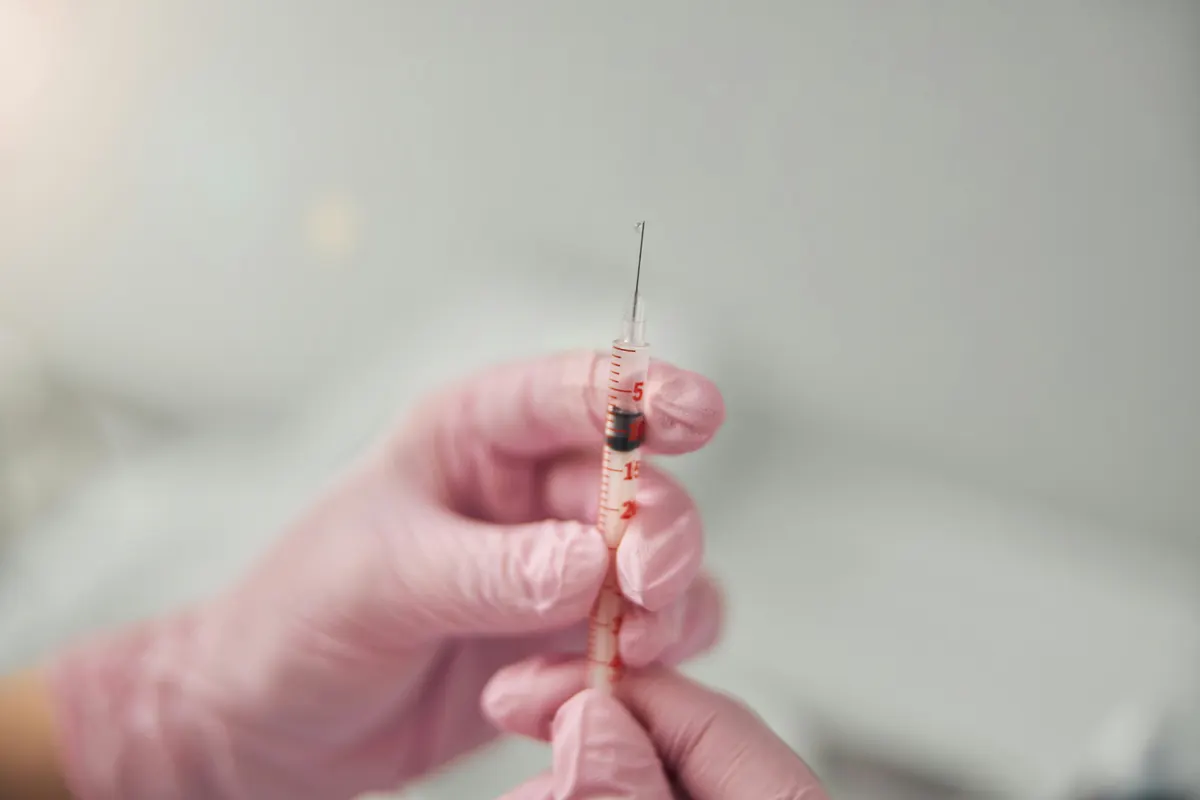 A blue-gloved injector holding a fine needle against the angle of a woman&rsquo;s jaw, just in front of the ear