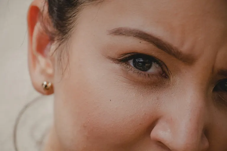 A close-up of a woman frowning, with vertical lines visible between her eyebrows