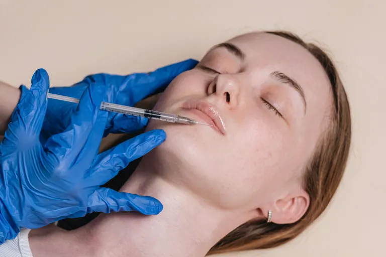 A gloved clinician injecting along the jawline and upper neck of a reclining patient