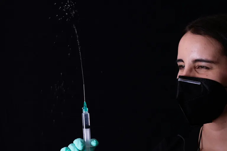 A syringe releasing a fine droplet, photographed against a dark background