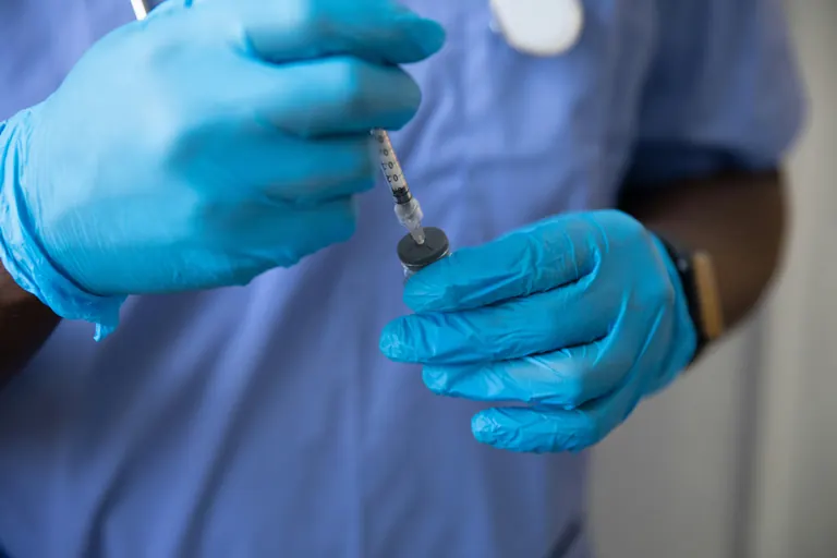 A healthcare worker in scrubs and gloves carefully drawing medication into a syringe