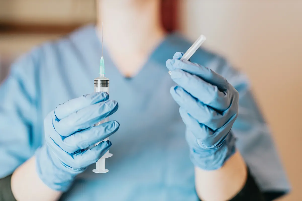 A clinician in blue gloves holding two prepared syringes, one in each hand