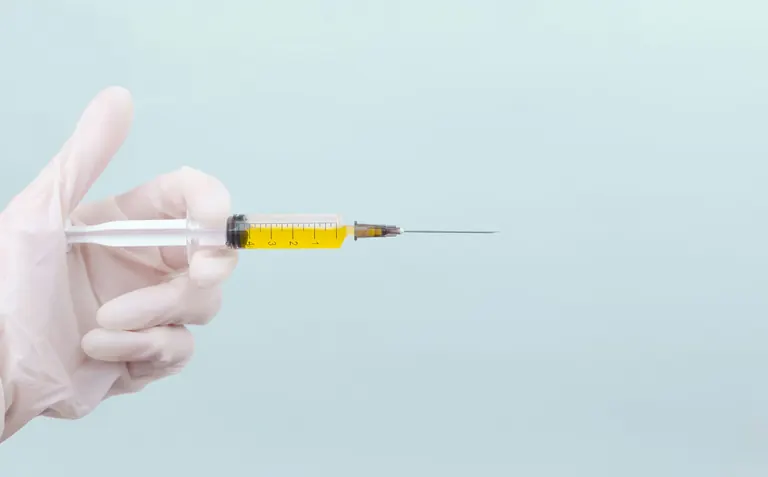 A gloved hand holding a prepared syringe of pale yellow solution