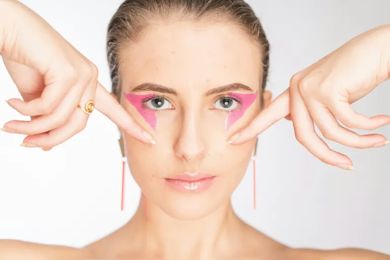 A woman using her fingertips to pull gently at the skin around her own eyes and cheeks