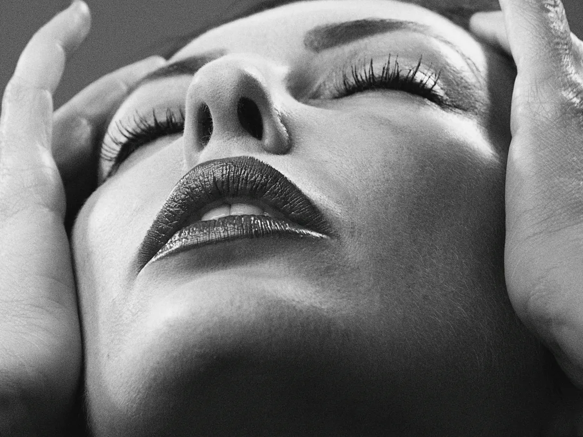 A purple-gloved injector steadying a patient&rsquo;s lower lip while placing a filler syringe at the lip border
