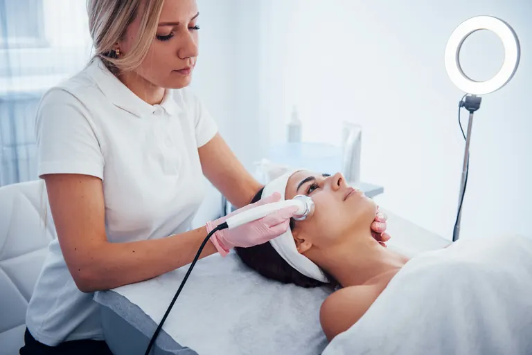 A clinician holding a handheld ultrasound treatment device against a patient’s face