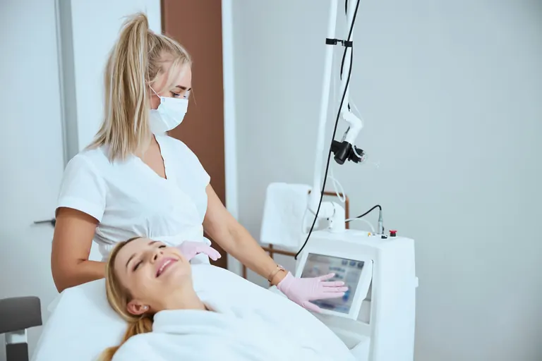 A patient lying under a laser treatment machine while a clinician operates it