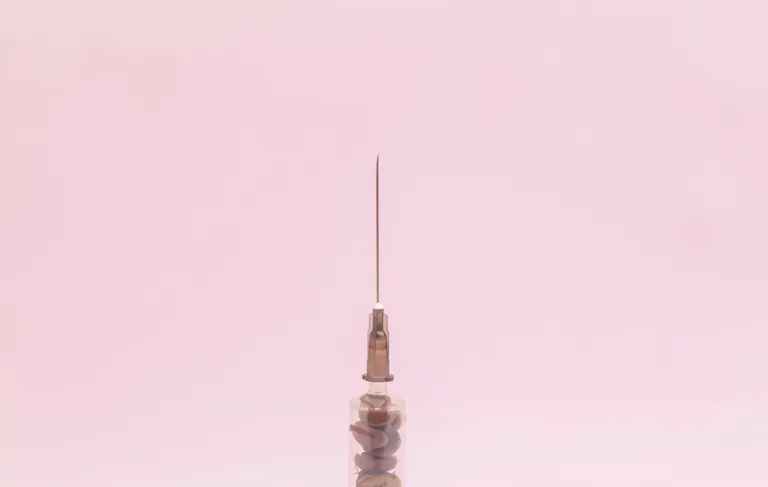 A single fine-gauge syringe photographed upright against a soft pink background