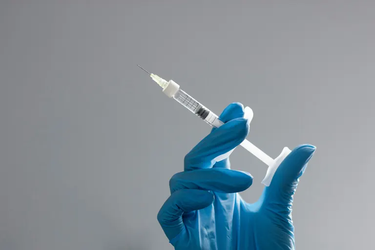 A blue-gloved hand holding a fine-gauge syringe