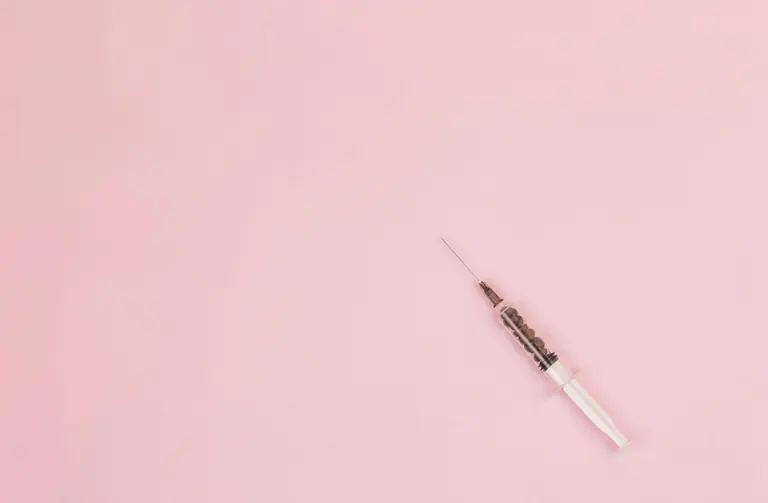 A prepared syringe lying diagonally across a plain pink background