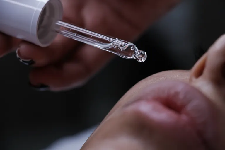 A close-up of a dropper releasing a drop of liquid onto skin in low light