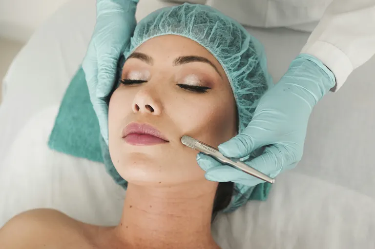 A gloved clinician working across the cheek of a reclining patient during a skin treatment