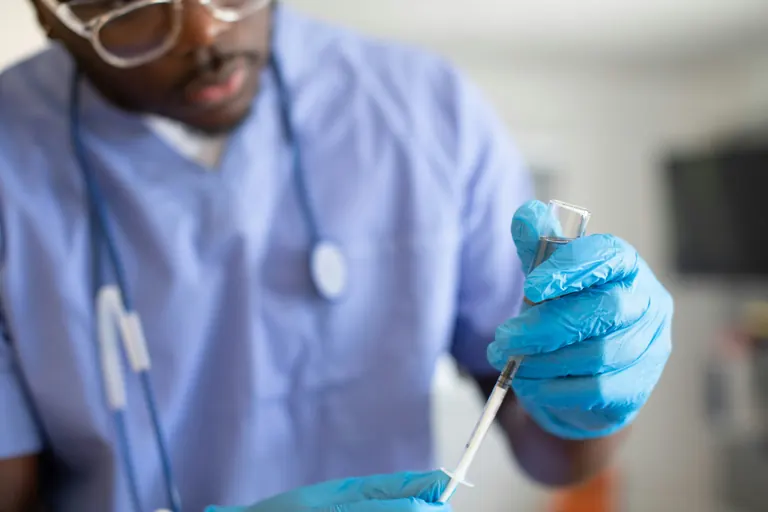 A clinician in scrubs drawing a dose into a syringe