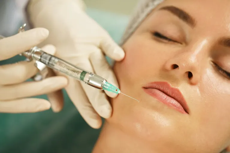 A gloved clinician injecting the mid-face of a reclining patient during a treatment