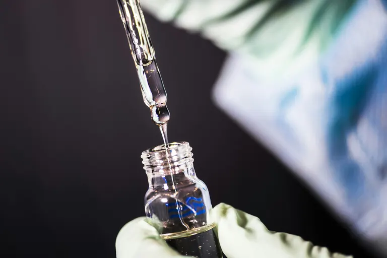 A glass dropper releasing a drop of serum back into its amber bottle