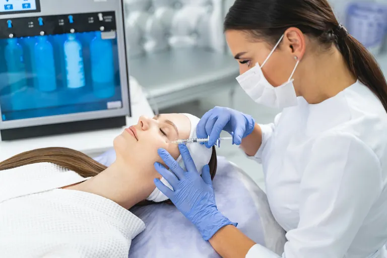 A clinician operating a skin-treatment device on a patient’s face beside a monitor