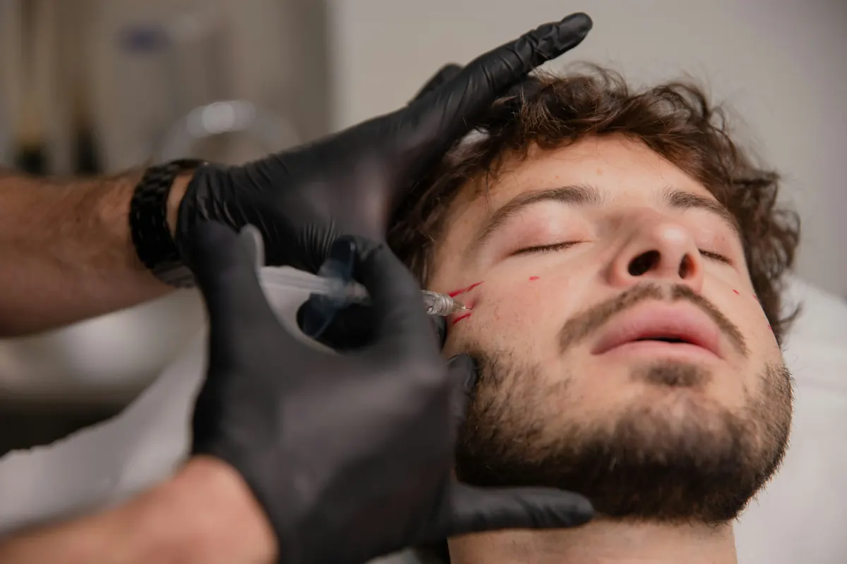 A black-gloved therapist applying a treatment to the face of a reclined male patient