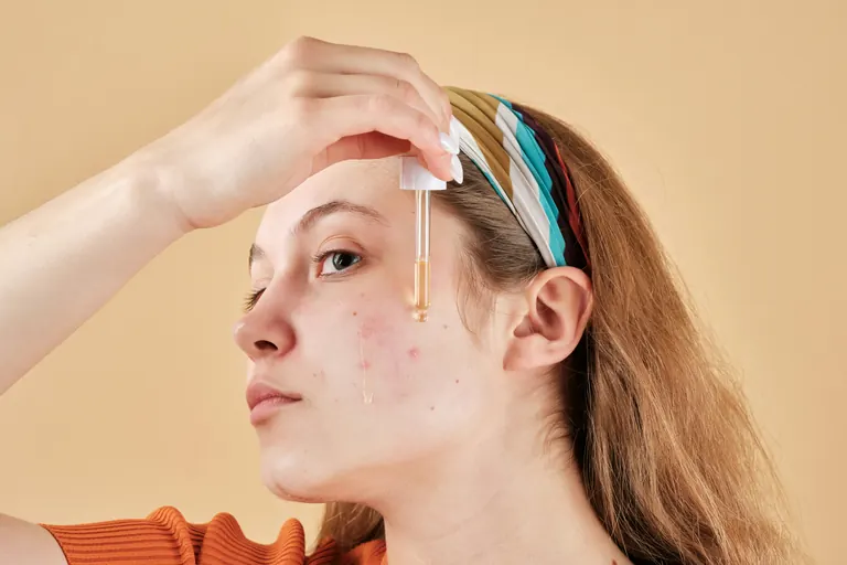 A woman applying a serum from a glass dropper to her own cheek and forehead