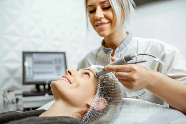 A clinician performing an ultrasound-guided facial treatment with a screen alongside
