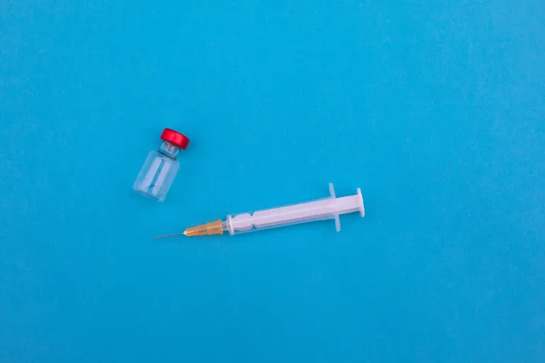 A single glass vial and a prepared syringe photographed on a plain blue background