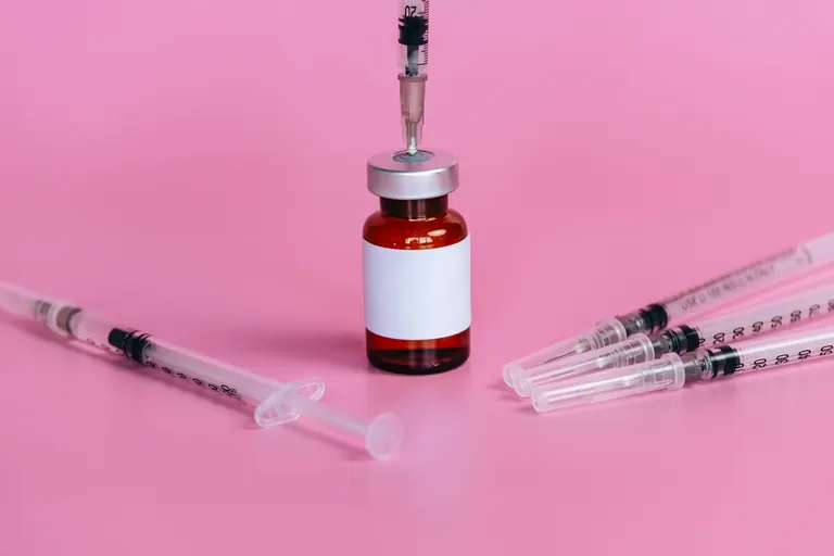 A medication vial standing between two prepared syringes on a pink background