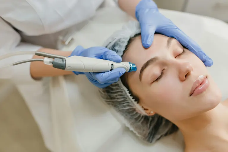 A gloved clinician moving a handheld skin treatment device across a patient&rsquo;s forehead