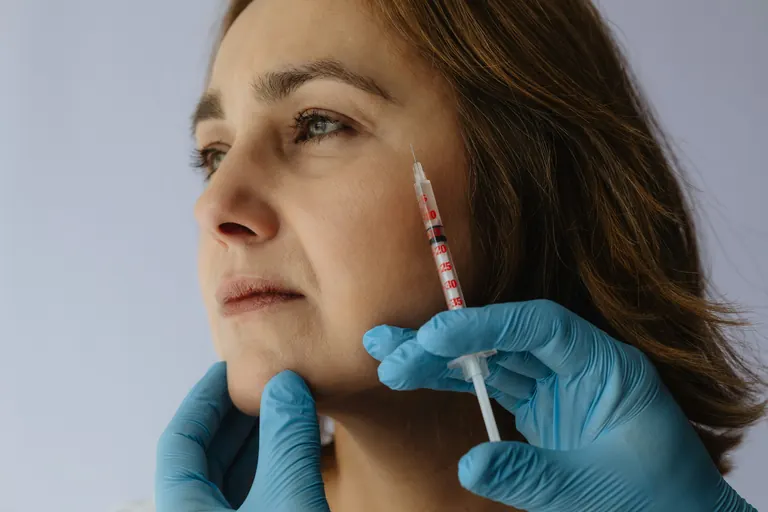 A graduated syringe with numbered unit markings held in gloved hands beside a patient&rsquo;s face