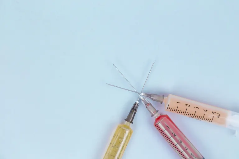 Two prepared syringes lying beside small glass medication vials on a pale blue surface