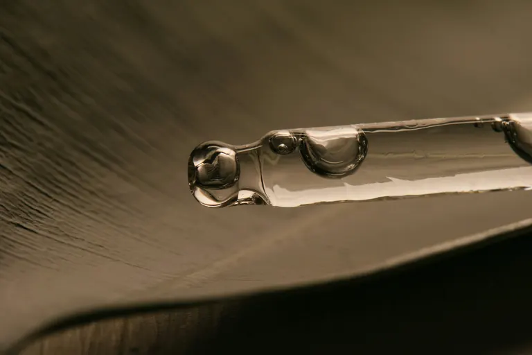 A glass pipette of clear serum resting on a dark surface, with no people in frame