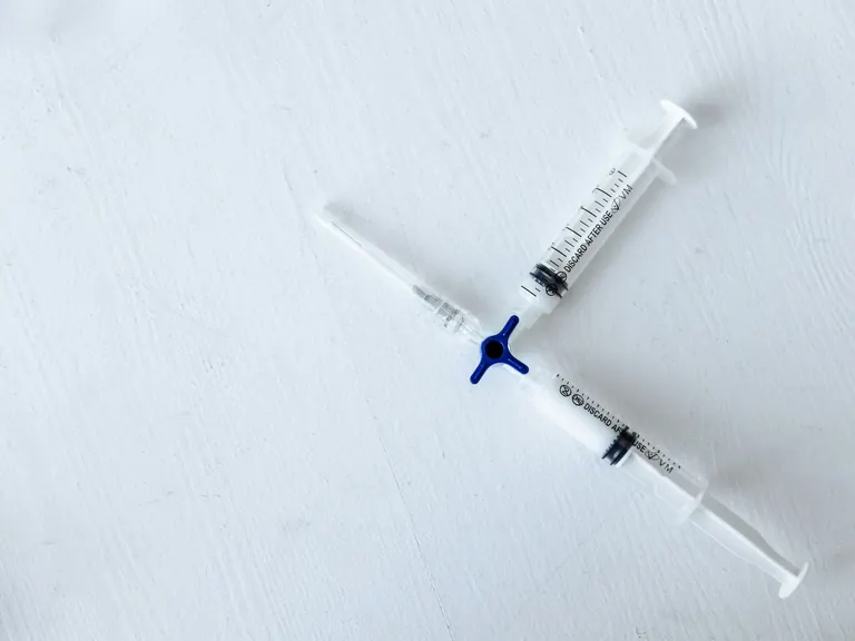 Two graduated syringes joined by a blue three-way coupler on a white surface, with &ldquo;discard after use&rdquo; printed along the barrels