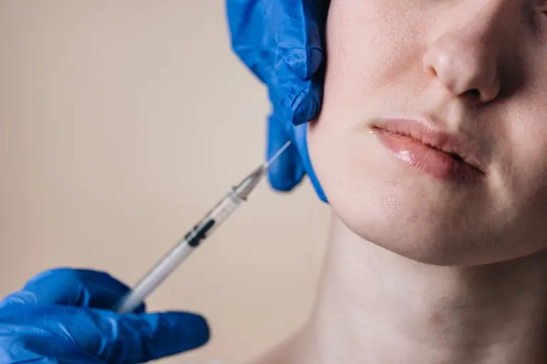 A blue-gloved clinician injecting along the jawline of a woman shown in profile