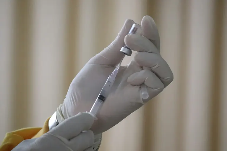 Gloved hands drawing solution from an inverted glass vial into a syringe