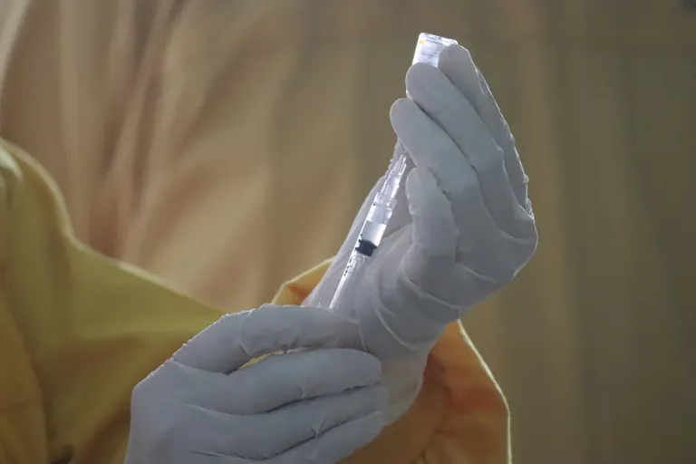 Gloved hands drawing solution from a small glass vial into a syringe